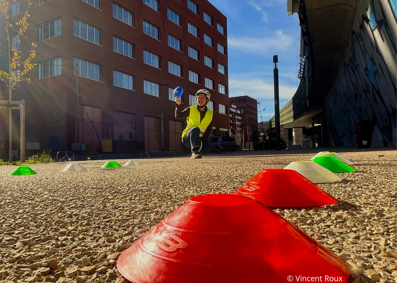 photo_pédagogie_site_pratique une éducatrice mobilité à vélo tenant une coupelle de couleur à la main lors d'un exercice de maniabilité à vélo pour un enfant